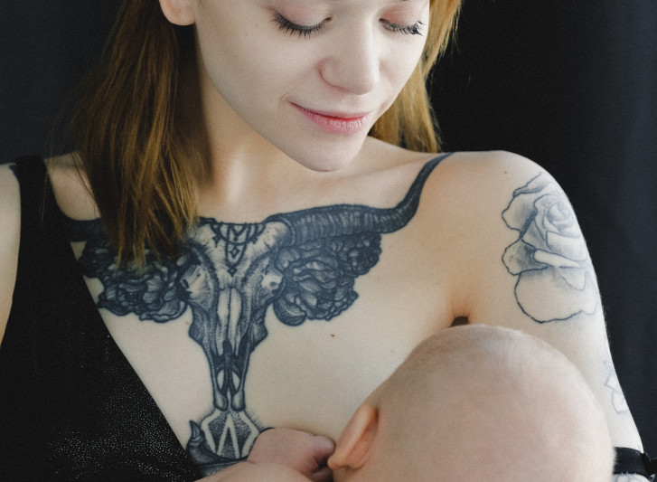 une femme tatouée allaite son bébé en le regardant